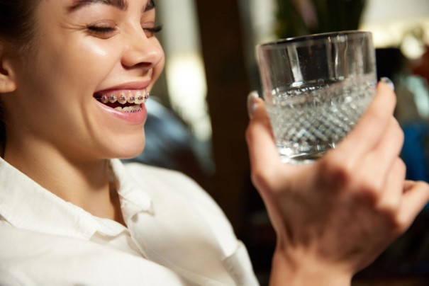Person mit Zahnspange hält ein Glas Wasser.